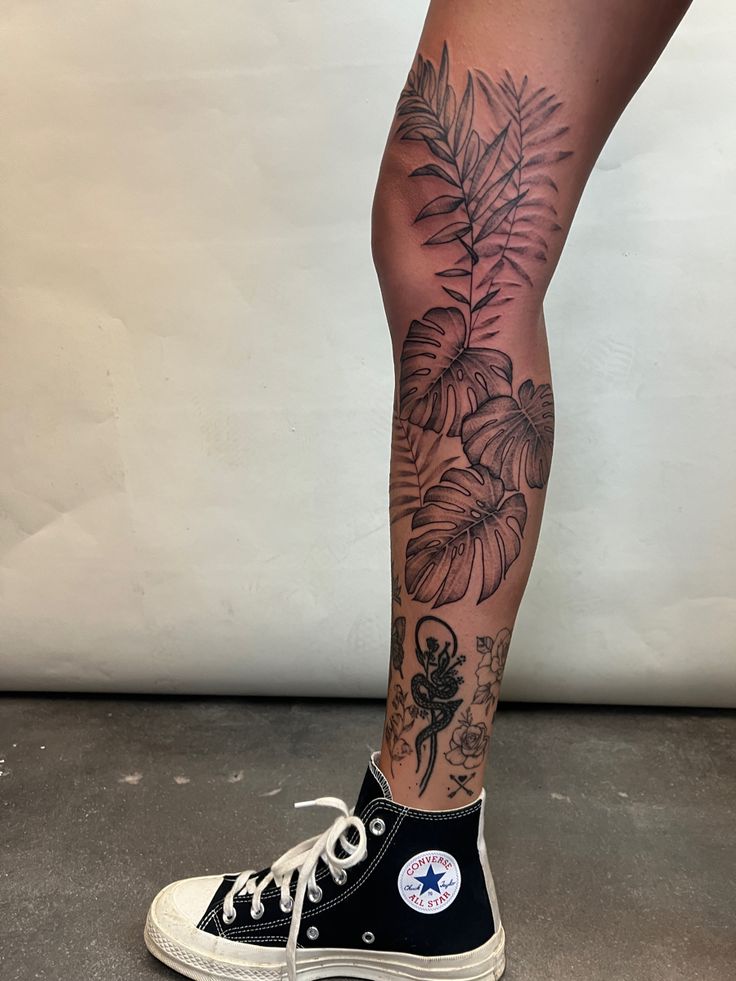 a woman's legs with tattoos and flowers on them, standing in front of a white wall