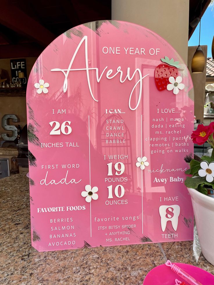 a pink sign sitting on top of a counter next to a potted plant with flowers