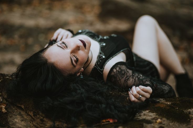 a woman laying on top of a rock next to a leaf covered forest floor with her eyes closed