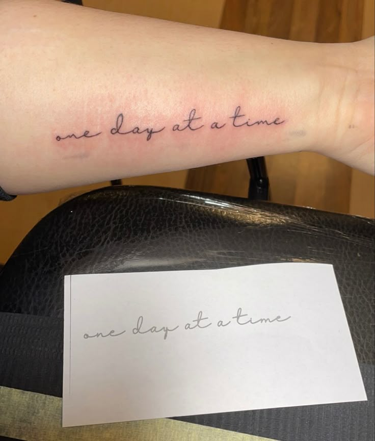 a woman's arm with the words one day at a time written on it