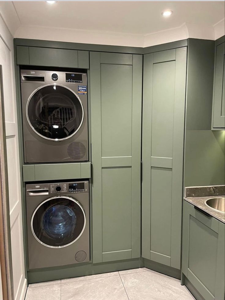 a washer and dryer are in the corner of this laundry room with green cabinets