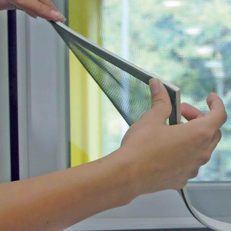 a person is holding something in their hand near a window with blinds on the windowsill