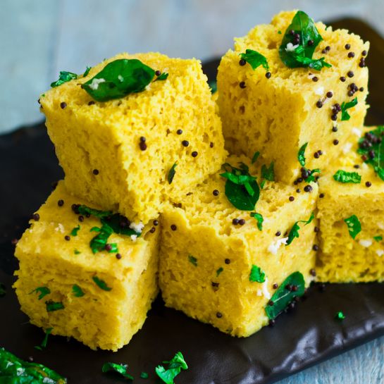 several pieces of food on a black plate with some green leaves around it and the words instant dhokla written above them