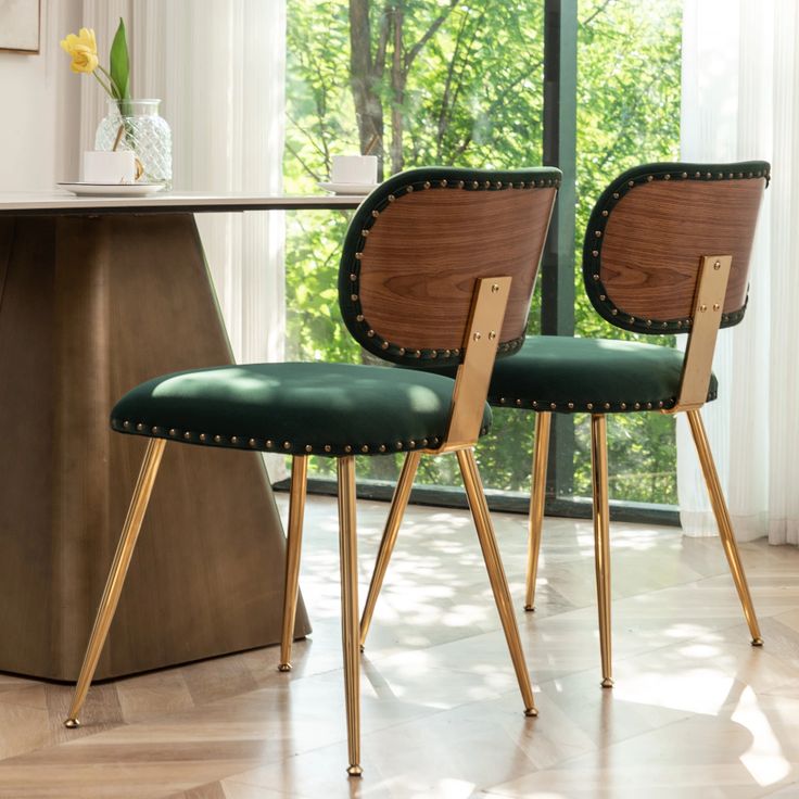 two wooden chairs with green upholstered seats sit in front of a table and window