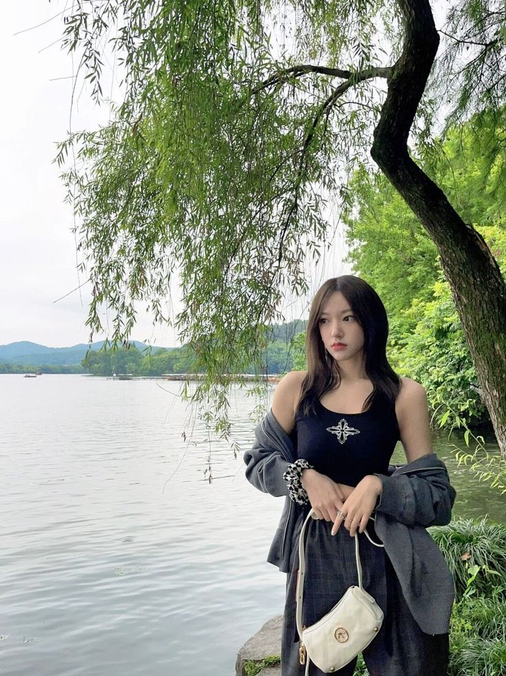 a woman standing next to a tree near the water