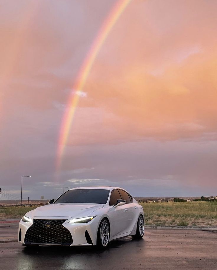 a white car is parked in front of a rainbow with a pink sky behind it