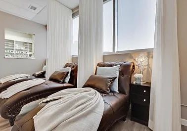 two brown leather couches sitting next to each other in a living room with large windows