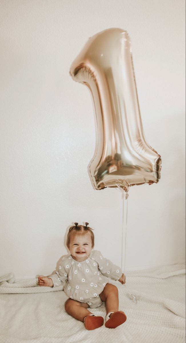 a baby sitting on a bed next to a balloon