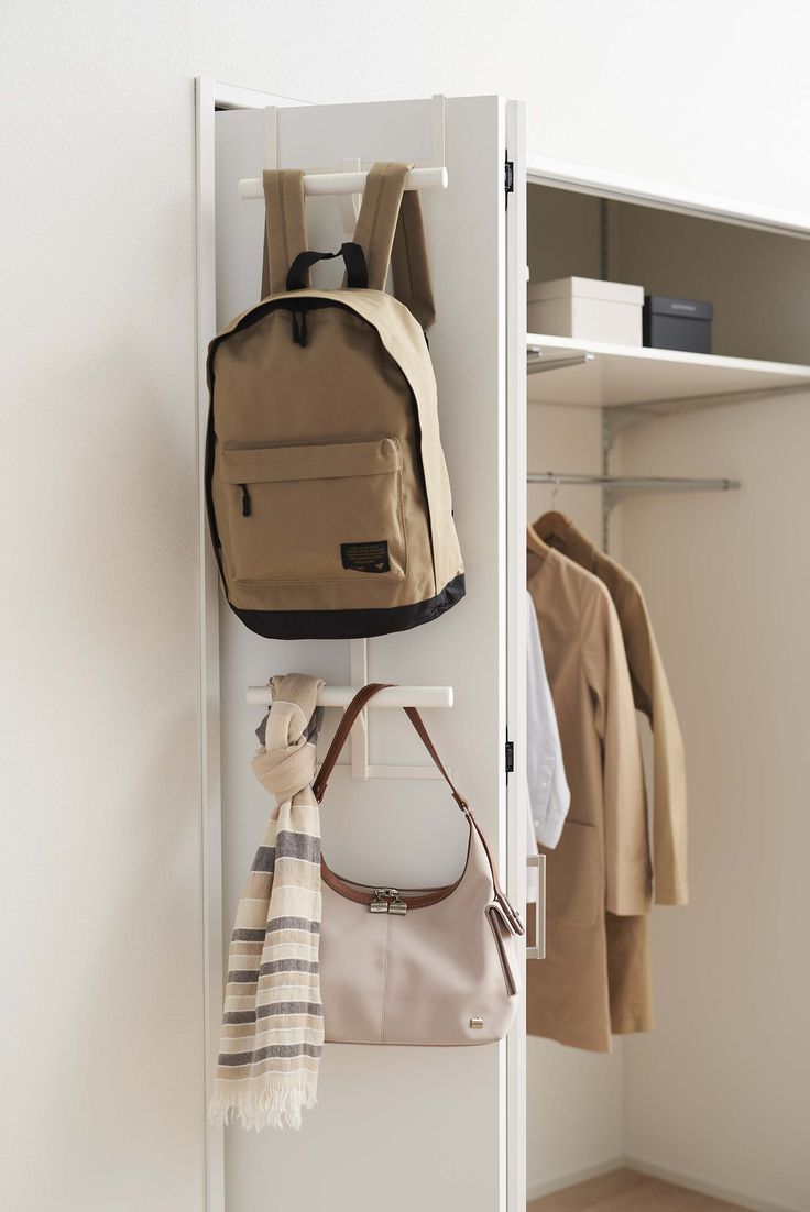 a white closet with a backpack and purse hanging on the wall