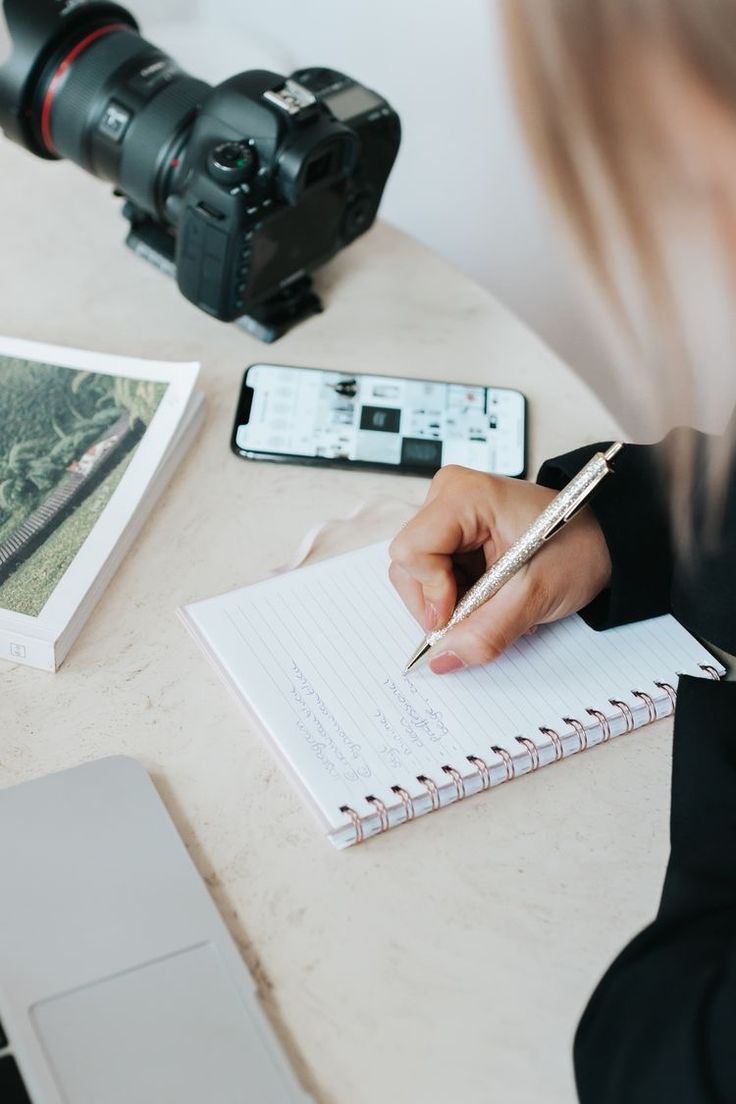 a person writing on a notepad next to a camera