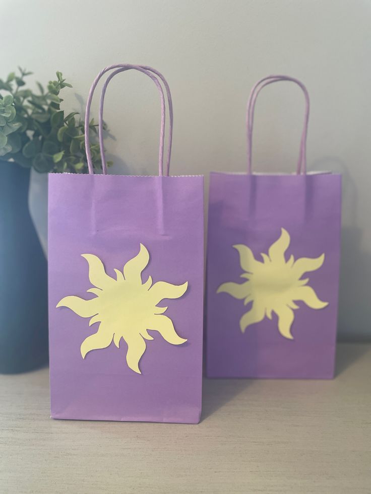 two purple bags with yellow flowers on them are sitting next to a potted plant