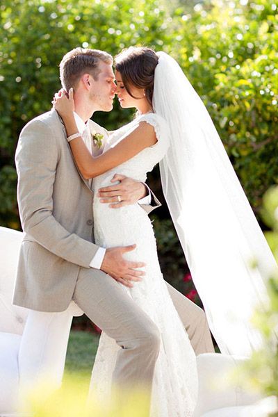 a bride and groom are kissing in front of some bushes at their outdoor wedding ceremony