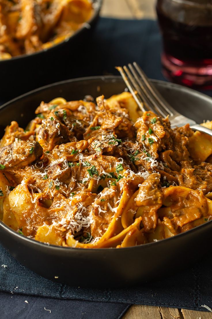 a pan filled with pasta and meat covered in sauce next to a glass of wine