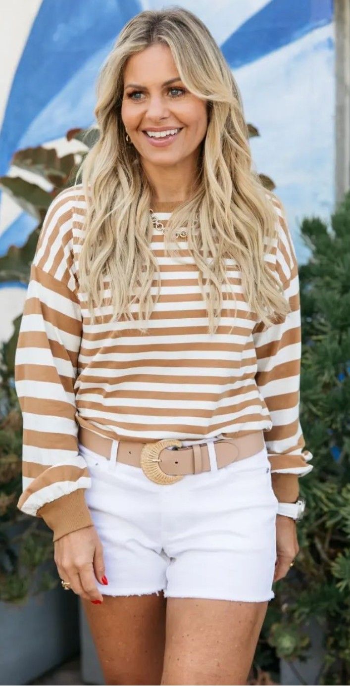 a woman with blonde hair wearing white shorts and a striped shirt smiles at the camera