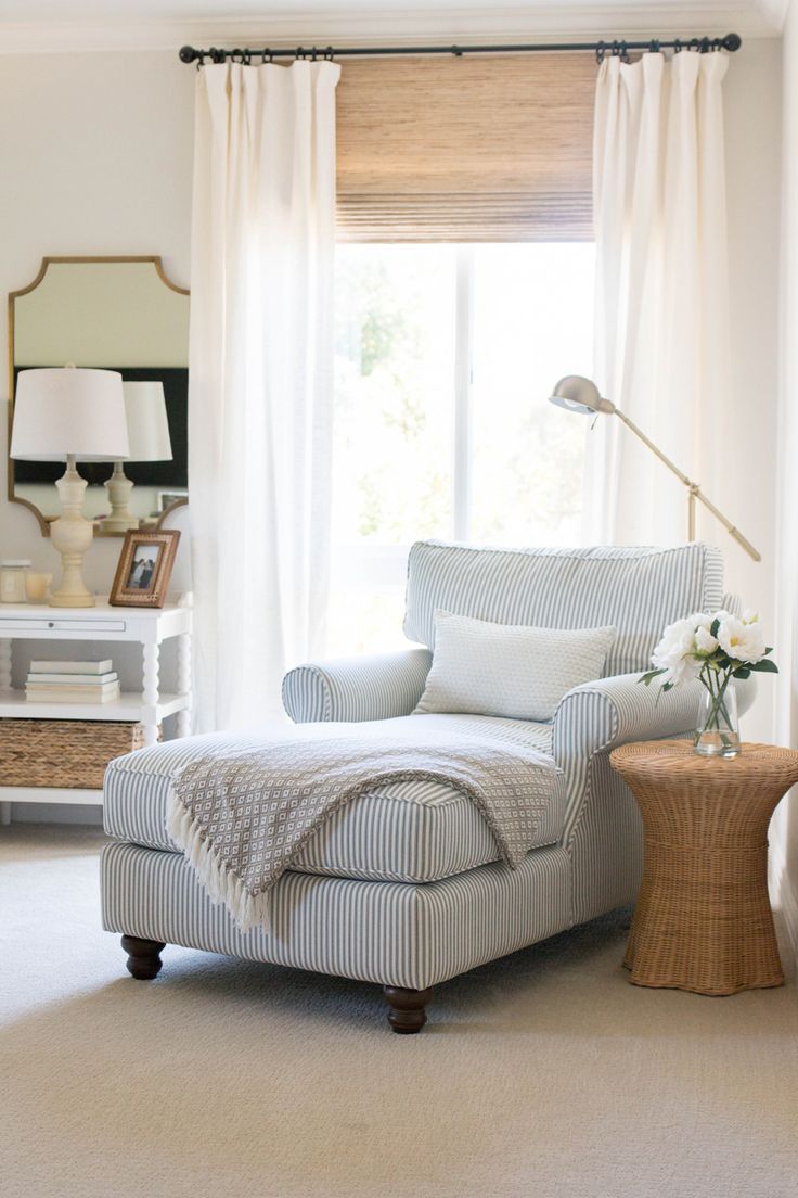 a living room with a chair, ottoman and lamp on the side table in front of a window