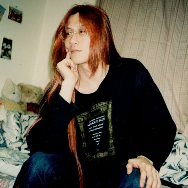 a woman sitting on top of a bed next to a teddy bear and wearing glasses