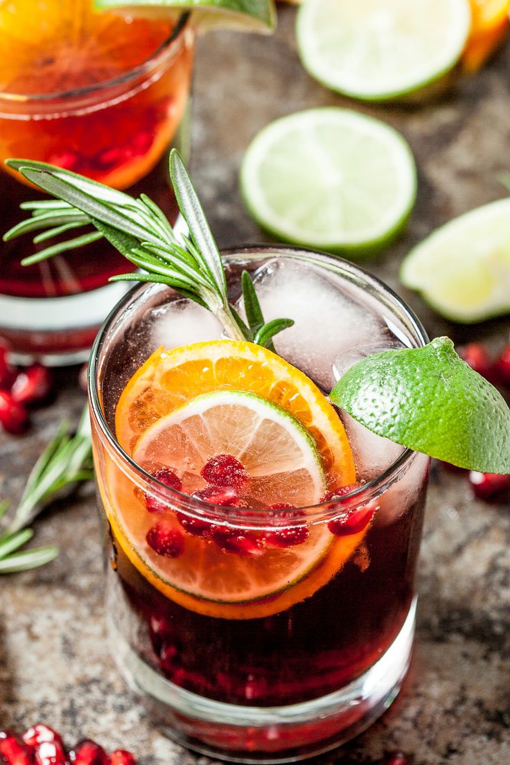 two glasses filled with cranberry punch and garnished with rosemary, oranges, and lime