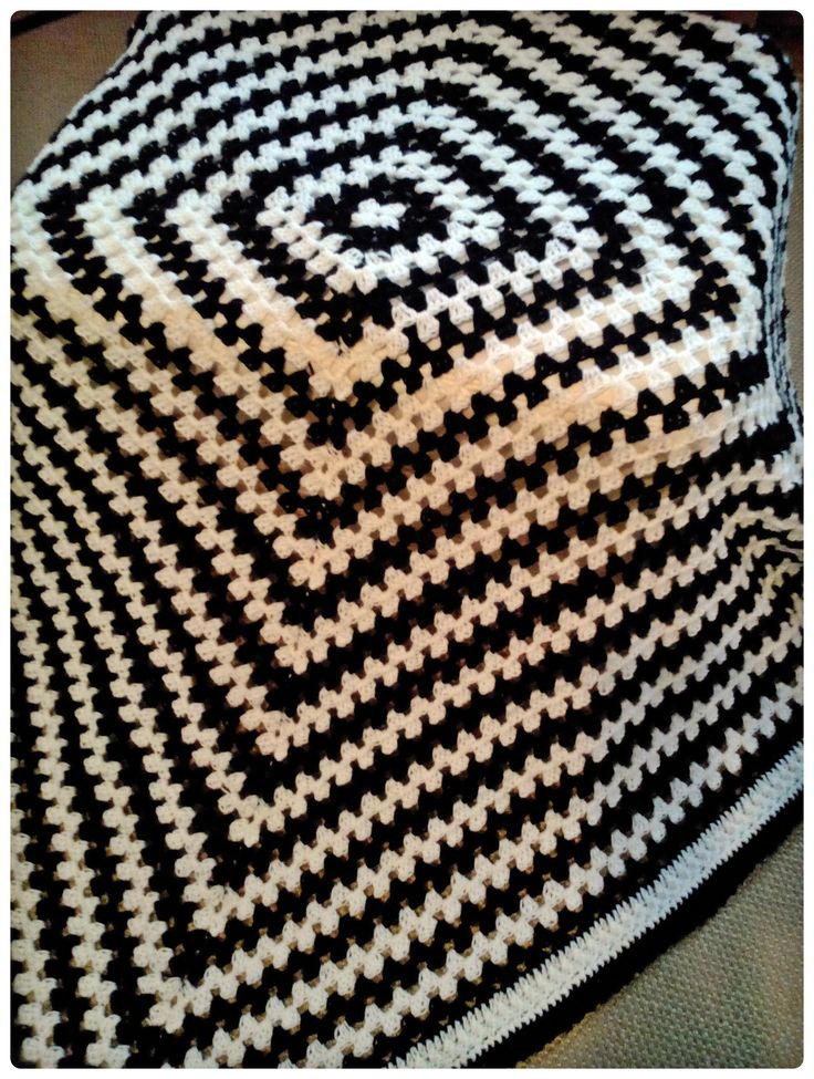 a black and white crocheted blanket sitting on top of a bed next to a pillow