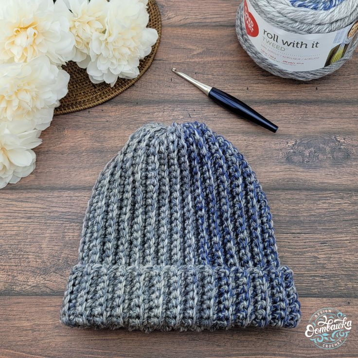 a knitted hat sitting on top of a wooden table next to yarn and flowers