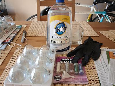 the table is covered with plastic cups and bottles of cleaning products, including gloves, water bottle, glue, paper towels, and other items