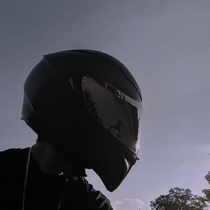 a person wearing a helmet and chain around their neck, with trees in the background