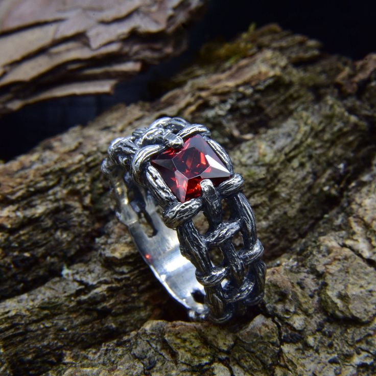 a silver ring with a red stone sitting on top of a tree branch in the woods