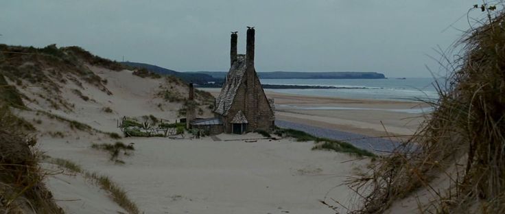 an old structure on the beach with grass growing out of it's sides and water in the background