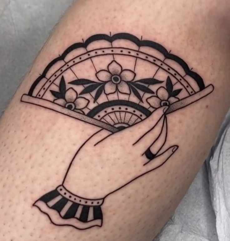 a woman's arm with a black and white tattoo design on it, holding a fan