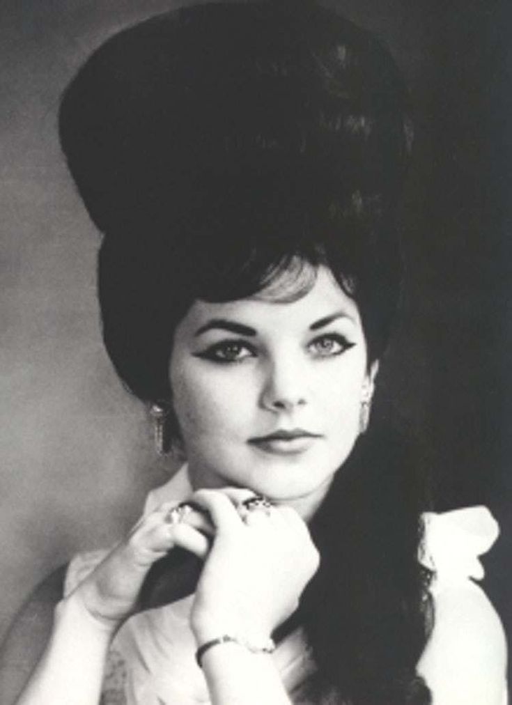 black and white photograph of a woman with long hair wearing an elegant dress, holding her hand to her chin