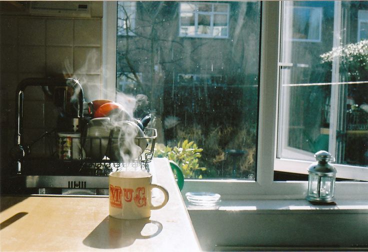 a coffee cup with steam rising from it sitting on a table in front of a window