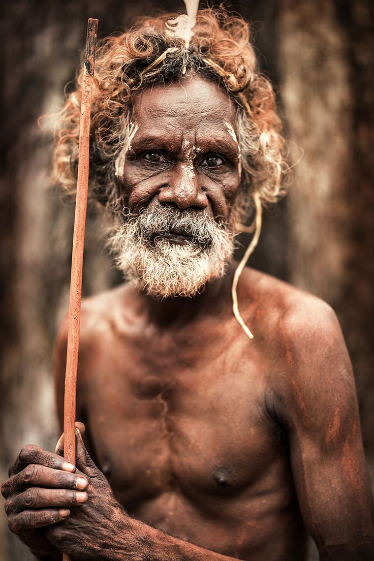 an old man with no shirt holding a stick in his hand and looking at the camera