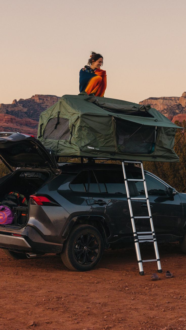 a woman sitting on top of a car with the hood open and luggage strapped to it