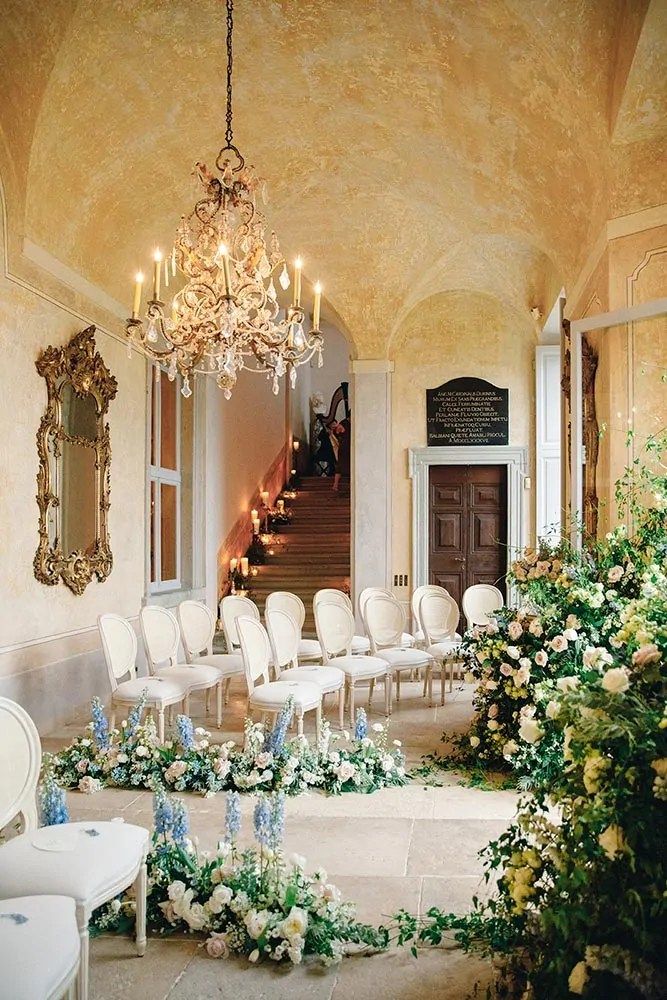 a room filled with lots of white chairs next to a chandelier and flowers