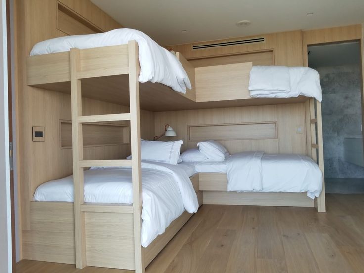 two bunk beds in a room with wood flooring and white linens on them