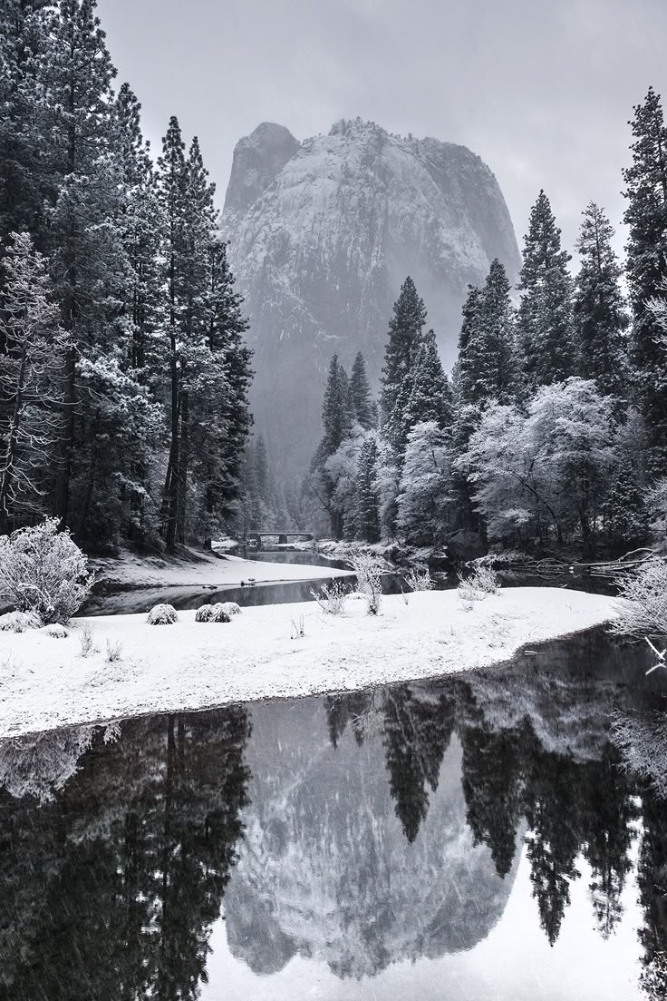 snow covered mountains and trees surrounding a small lake in the middle of a snowy forest