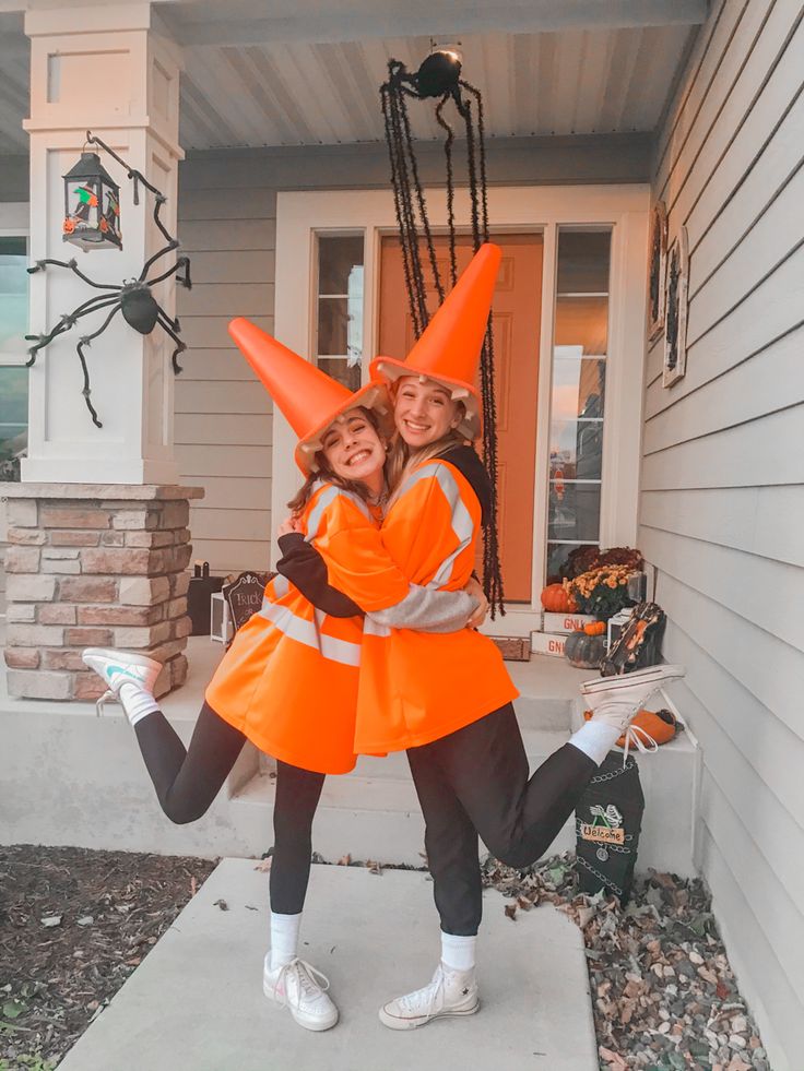 two girls in orange jackets and black pants are posing for the camera outside their house