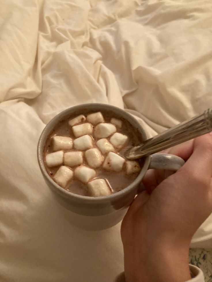 a person is holding a spoon over a cup of hot chocolate with marshmallows