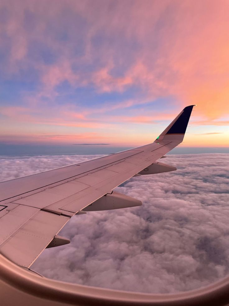 the wing of an airplane as it flies above the clouds at sunset or dawn with pink and blue hues