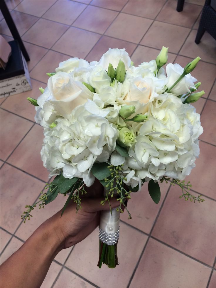 a person holding a bouquet of white flowers in their hand on a tile floored area