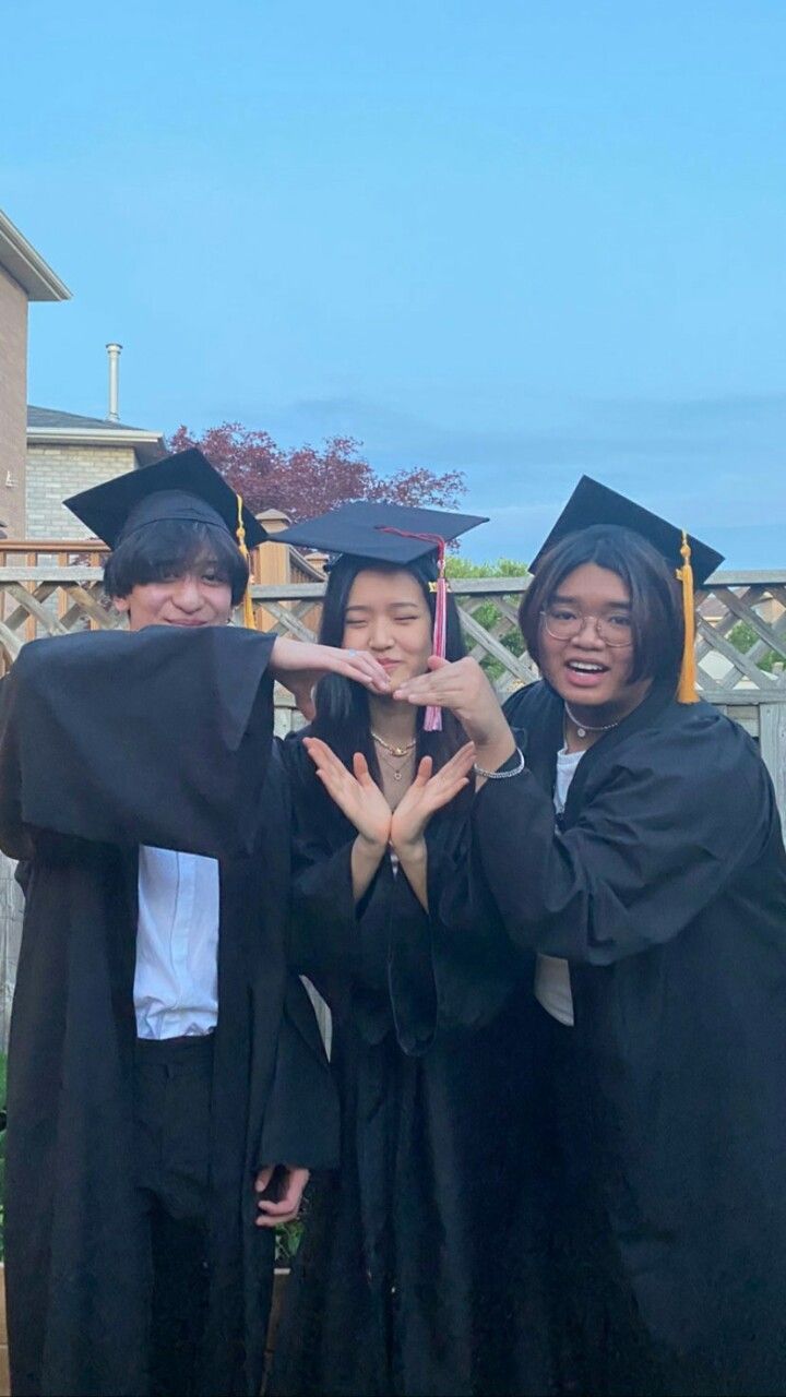 three people in graduation gowns making the v sign with their hands while standing together