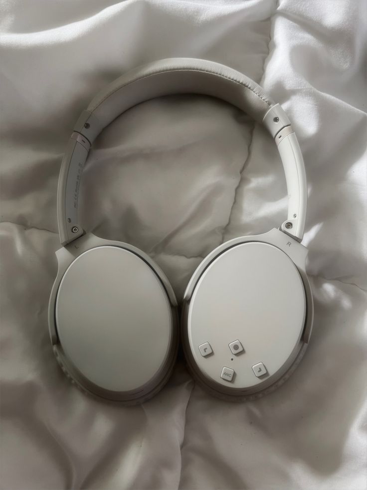 two white headphones laying on top of a bed