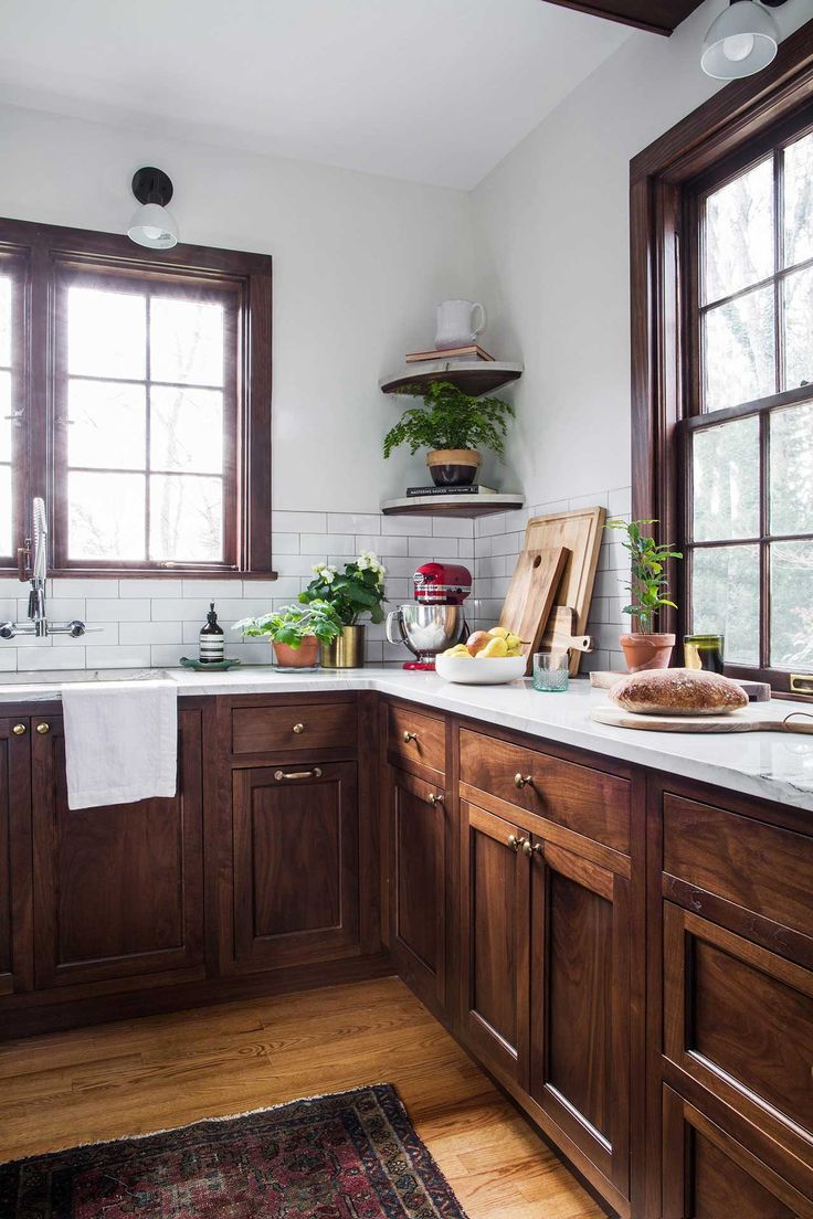 a kitchen with wooden cabinets and white counter tops, along with potted plants on the window sill