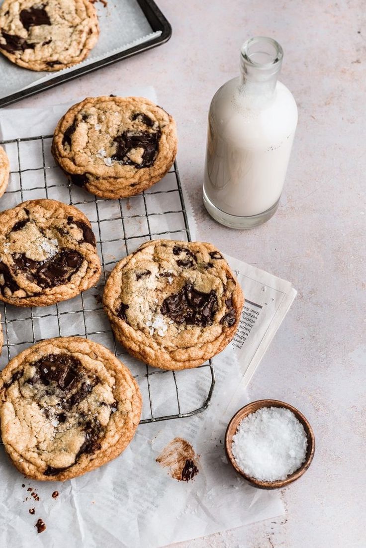 chocolate chip cookies cooling on a wire rack next to a glass of milk and spoons