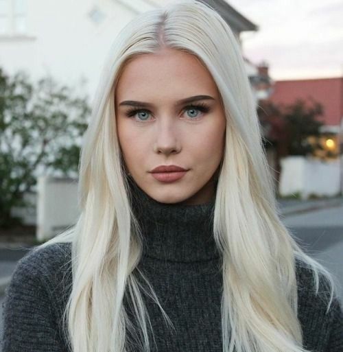 a woman with long blonde hair standing in front of a street and looking at the camera