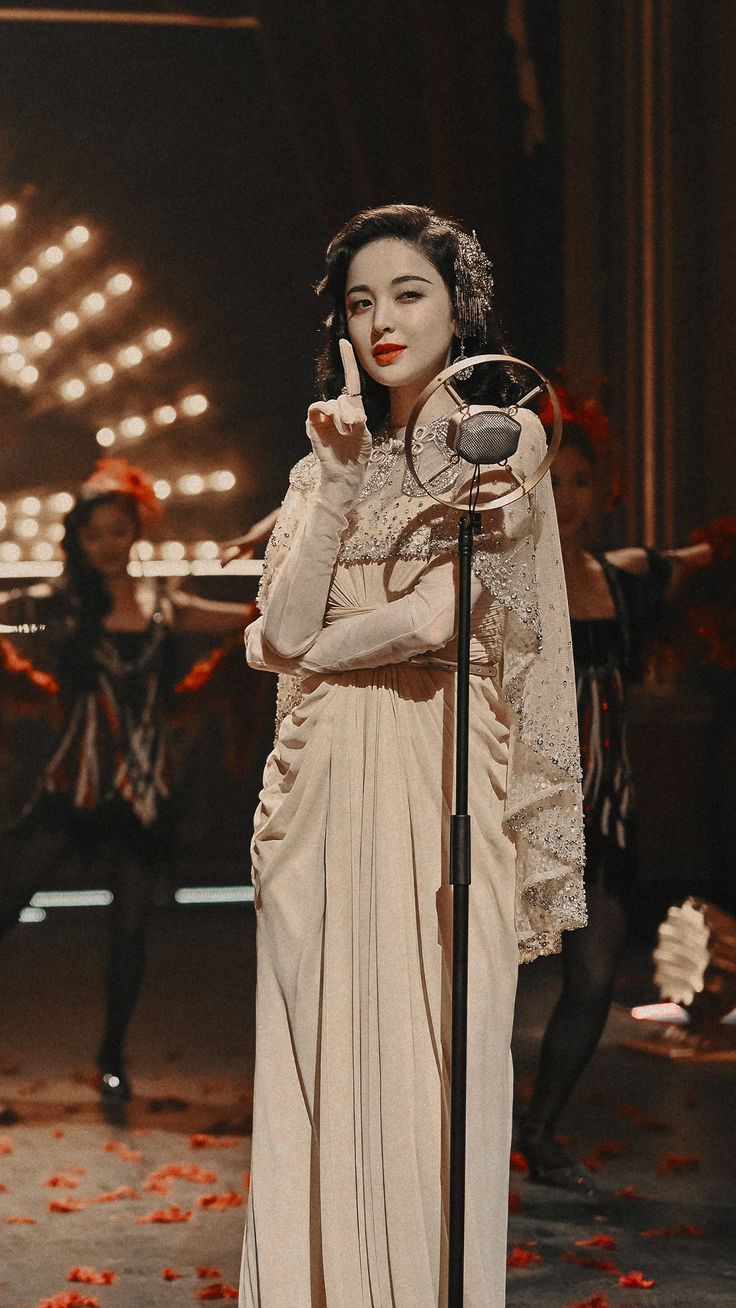 a woman standing next to a microphone on top of a stage with other people in the background