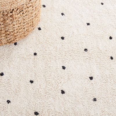 a white rug with black dots on it and a basket sitting next to the rug