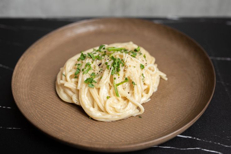 a brown plate topped with pasta and garnished with parsley next to a black table