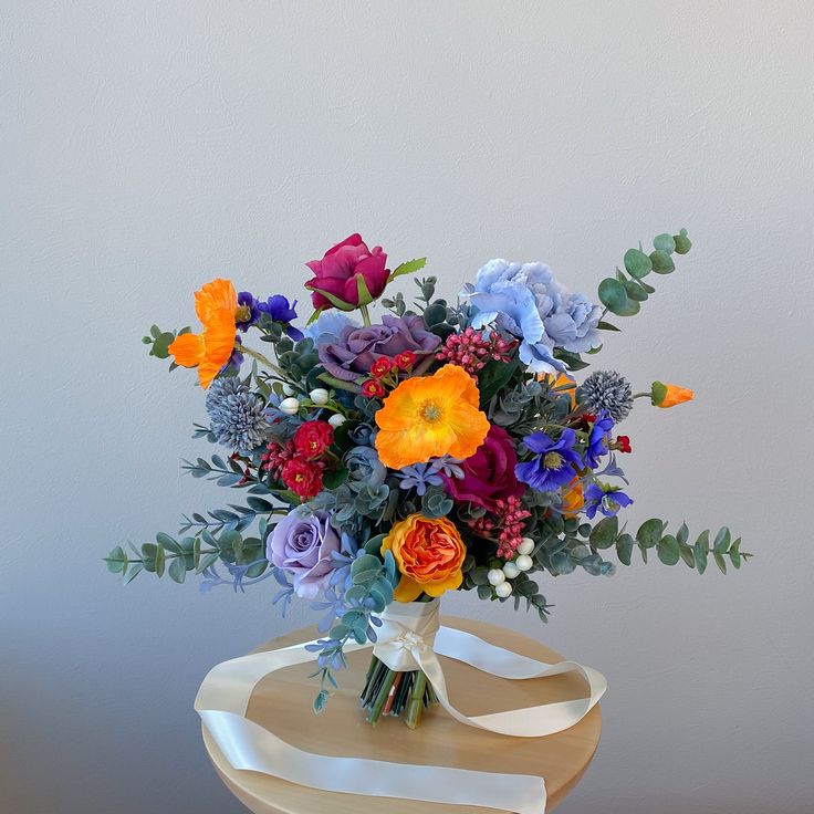 a vase filled with colorful flowers sitting on top of a wooden table next to a white wall