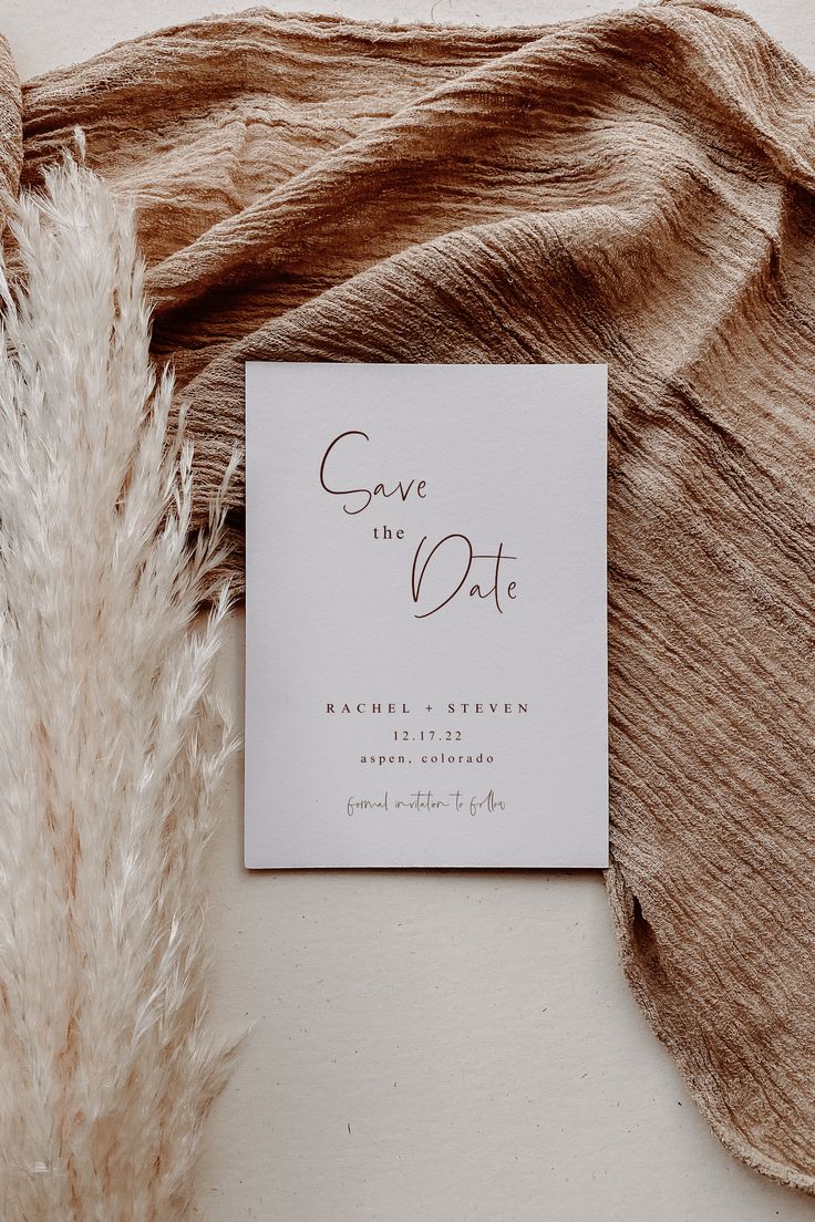 save the date card on top of a piece of fabric next to a pile of feathers