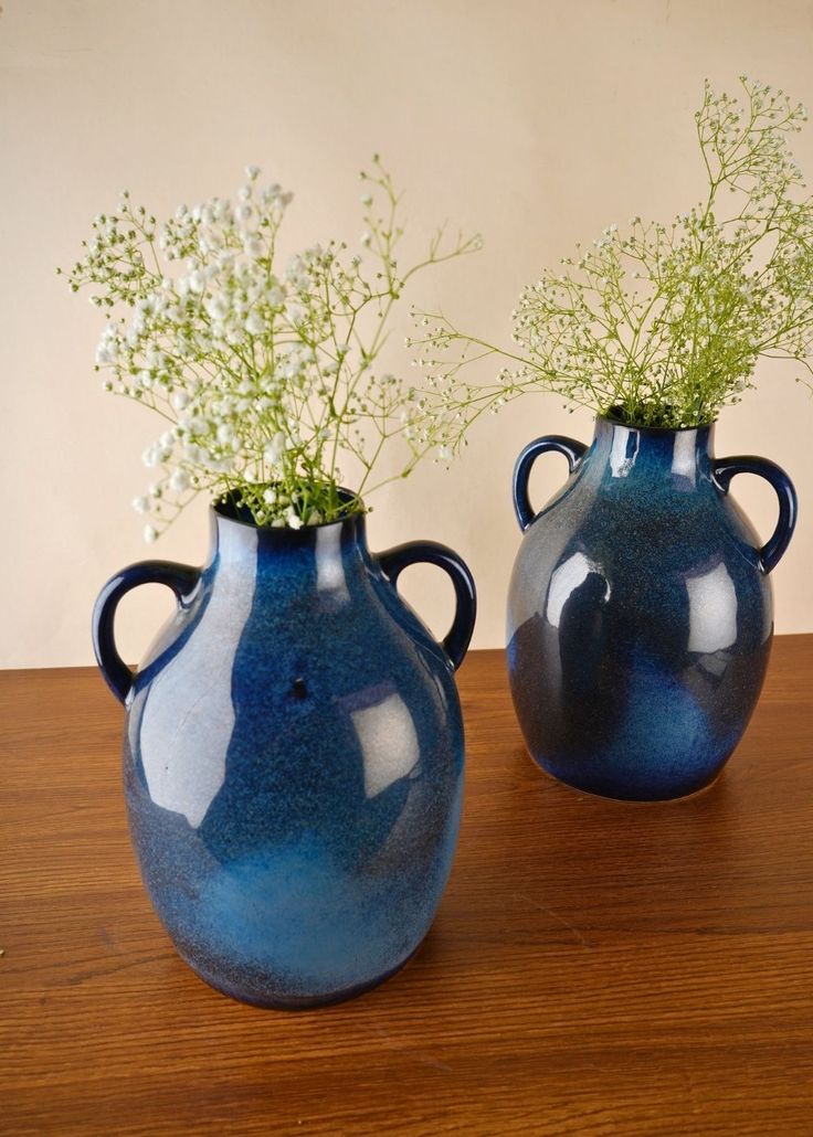 two blue vases sitting on top of a wooden table with flowers in each one